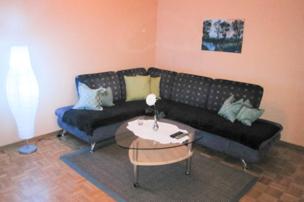 Wohnzimmer. Eine Couch zum es sich gemtlich machen. Mit Flachbildfernsehen kleinem Tisch sowie einer Stehleuchte.